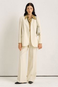 Woman in a cream suit and olive shirt posing indoors