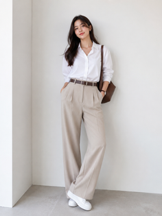 Woman in a white shirt and wide leg pants posing against a white wall