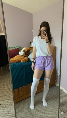 Woman in a white t-shirt, purple shorts, and thigh-high socks taking a mirror selfie