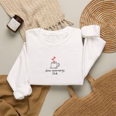White sweatshirt with 'slow mornings club' graphic, surrounded by cozy items