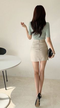 Woman with long dark hair wearing a light green top and a beige mini skirt