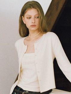 Young woman with long hair wearing a white cardigan and pearl necklace