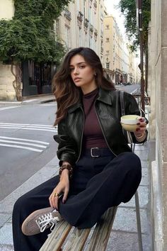 Woman with long hair in a leather jacket sitting on a bench on a city street