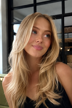 Woman with blonde layered hair and blue eyes in an indoor setting
