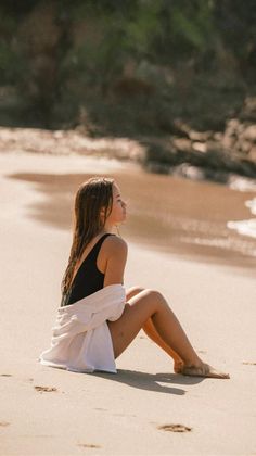 Woman in a black swimsuit and white shirt sitting on a sandy beach