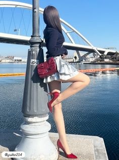 Woman in a silver skirt and red heels posing by a lamppost near water