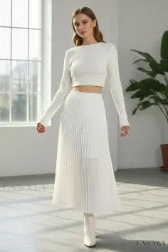 Woman in a white crop top and pleated skirt standing indoors