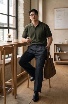 Man in a green polo shirt and pleated pants holding a phone in a cafe