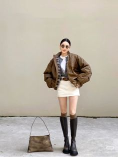 Woman in a brown jacket, white mini skirt, and knee-high boots standing outdoors