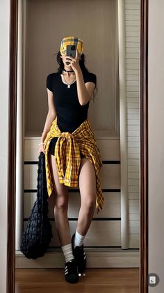 Person in a black top and plaid shirt tied around the waist taking a mirror selfie