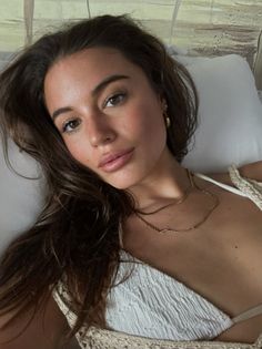 Woman with long brown hair and gold jewelry wearing a white top indoors