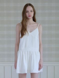 Woman in a white dress standing against a plaid wallpaper background