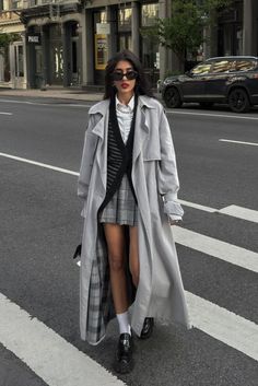 Woman in a long trench coat and plaid skirt walking on a city street