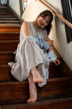 Woman in a long dress sitting barefoot on wooden stairs, smiling at the camera