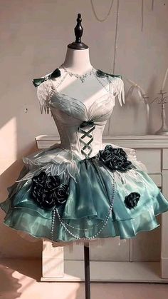 Elaborate teal and white ball gown with black roses and a pearl necklace on a mannequin