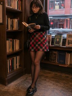 Woman in a plaid skirt and turtleneck reading a book in a bookstore