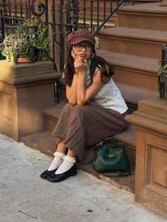Woman in a plaid skirt and newsboy cap sitting on outdoor steps