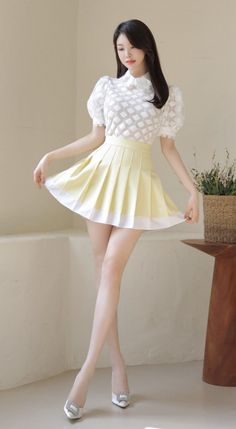 Woman in a white blouse and yellow pleated skirt posing indoors