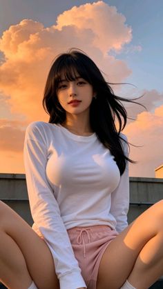 Woman with long black hair in a white long sleeve shirt and pink shorts at sunset