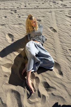 Blonde woman in a striped shirt and sweatpants lying on a sandy beach