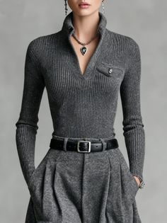 Woman in a gray ribbed sweater and pleated skirt with a black belt and silver jewelry