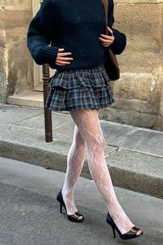 Person in a plaid skirt, white lace tights, and black sweater walking on a street