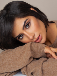 Woman with short dark hair in a brown sweater, resting her head on her arms