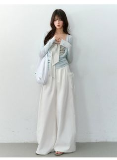 Woman with long hair wearing a light blue top and white wide-leg pants indoors