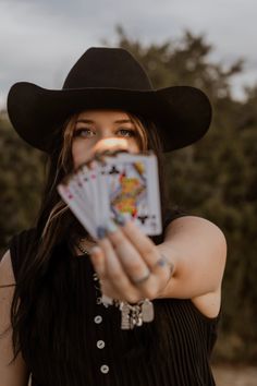 Woman in a cowboy hat holding playing cards towards the camera
