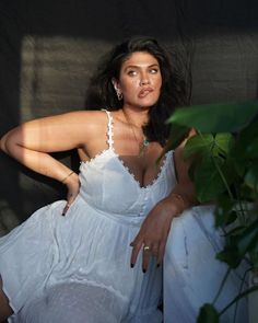Woman in a white dress with cleavage and jewelry, posing indoors with dramatic lighting