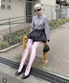 Person with short blonde hair and sunglasses wearing a black skirt and pink tights