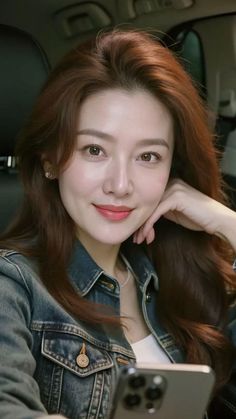 Woman with long brown hair wearing a denim jacket and pearl necklace, holding a phone