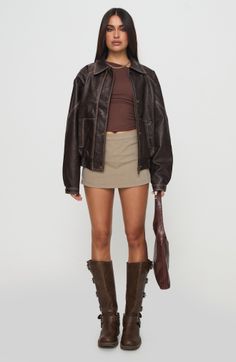 Woman in a brown leather jacket, mini skirt, and knee-high boots holding a handbag