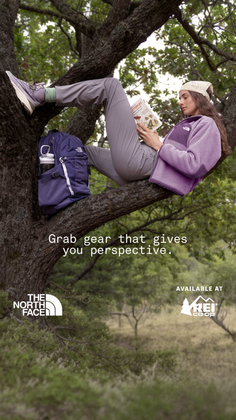 Woman in hiking gear reading a book while sitting on a tree branch