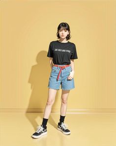 Woman with short hair wearing a black t-shirt and denim shorts with a red belt