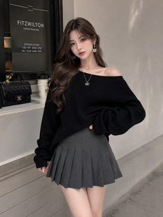 Woman with long hair wearing an off-shoulder sweater and pleated skirt outdoors