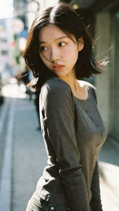 Woman with short black hair in a long sleeve shirt outdoors with backlight