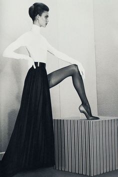 Woman in a white turtleneck and long black skirt posing in a studio