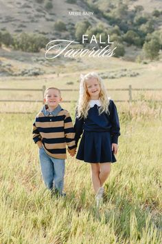 Two children holding hands in a green field with hills in the background