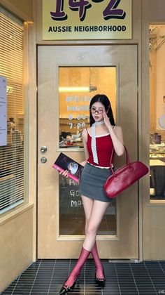 Woman in a red tank top and mini skirt holding a book and a red handbag