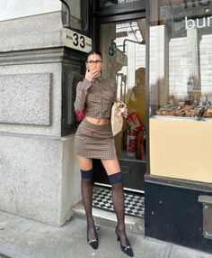 Woman in a plaid skirt and crop top with thigh high stockings on a city street