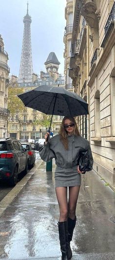 Woman in a grey outfit holding an umbrella on a rainy street with the Eiffel Tower in the background