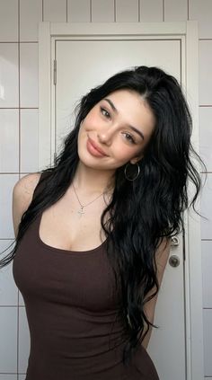 Woman with long black hair wearing a brown tank top and cross necklace