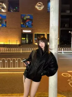 Woman in a black jacket and shorts posing on a street at night