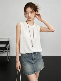 Woman in a white sleeveless top and denim skirt posing in a studio