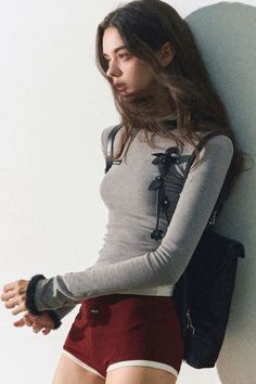 Woman with long hair wearing red shorts and a gray long sleeve top indoors