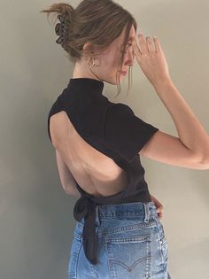 Woman in a black open-back top and denim jeans with hair in a bun