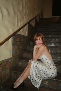 Woman in a polka dot dress sitting on stairs with her head resting on her hands