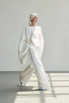Woman in a white oversized outfit and head scarf walking indoors