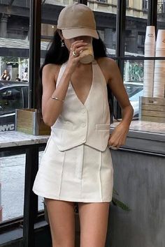 Woman in a white sleeveless top and mini skirt drinking from a cup indoors
